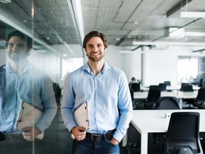 A portrait of young businessman standing in an office, looking at camera.